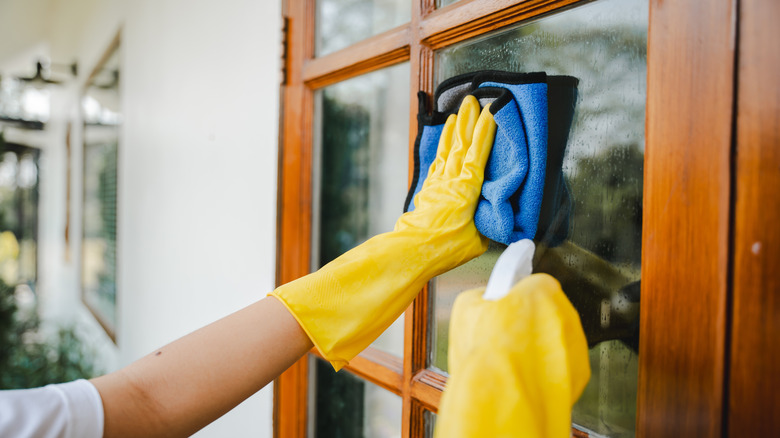 Person cleaning exterior door window with a microfiber cloth and spray