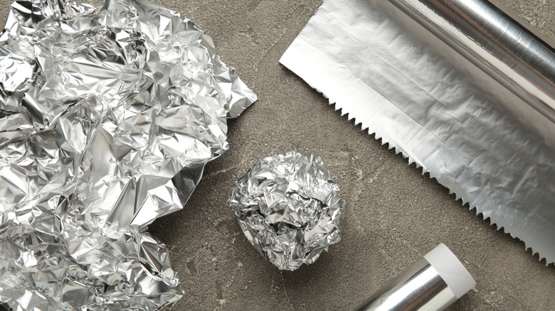 Crumpled aluminum foil sheets and a foil ball placed next to a roll of aluminum foil