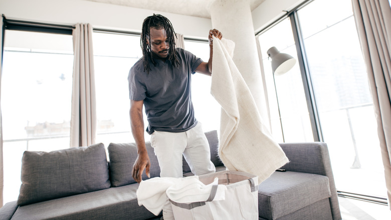 An African American man pulls linens from a laundry basket.