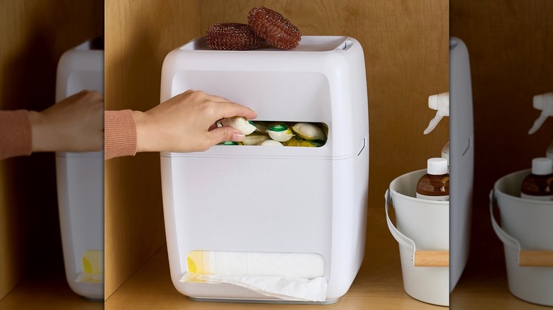 Hand taking a dishwasher pod out of the SinkSuite garbage bag and dishwasher pod dispenser