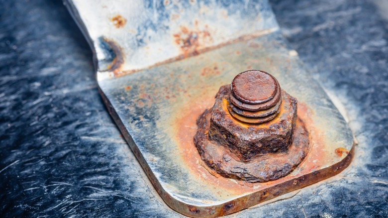 A close-up shot of a rusty bolt and nut secured to a metal plate