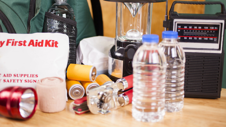 Emergency supplies on a table, with a battery-operated radio, bottled water, batteries, and a lantern on display