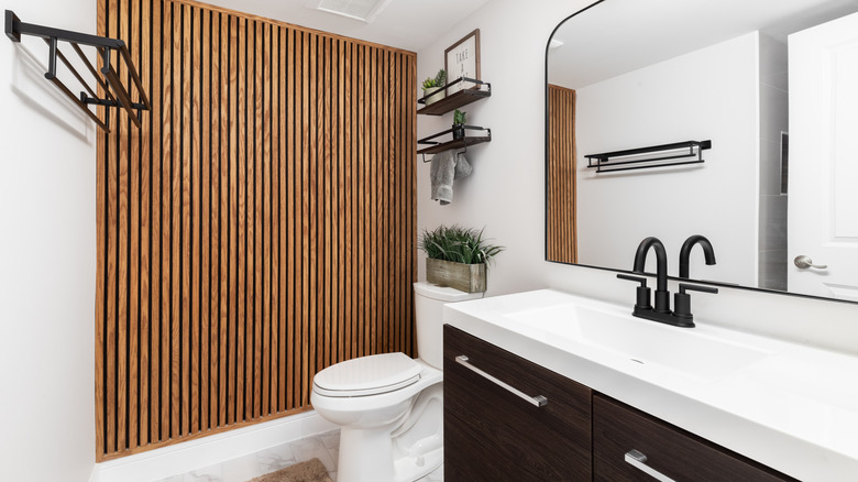 A bathroom with a dark wood cabinet, floating shelves with decorations above the toilet