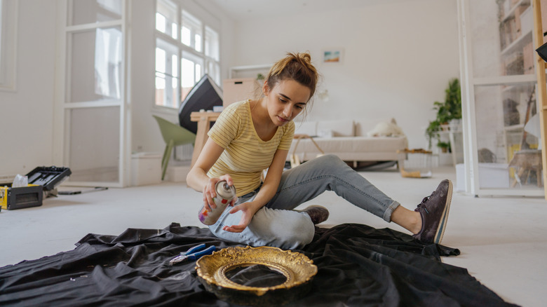 Person spray-painting a mirror on the floor of an appartment