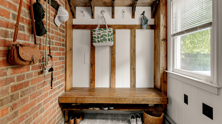 rustic entryway with exposed brick, wooden bench and multiple hooks to hang personalized items