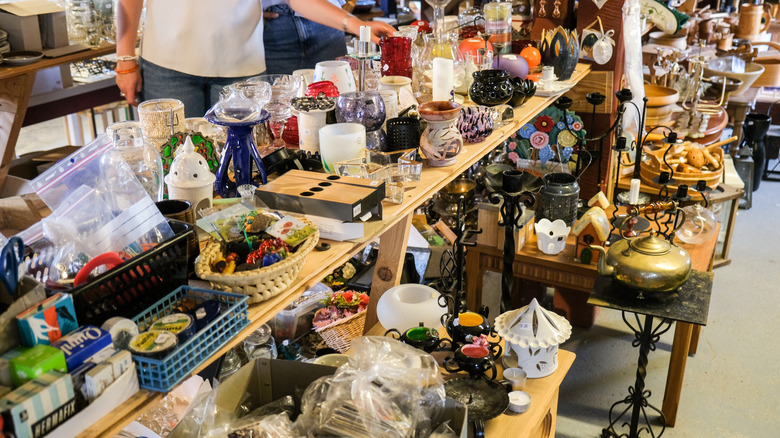 Person browsing thrift store table full of assorted items, from glassware to tape