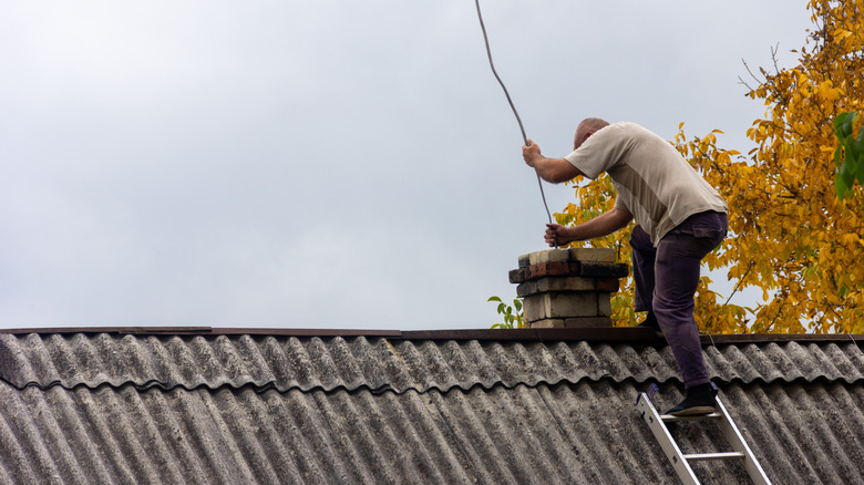 Man cleaning a chimney while standing on the roof