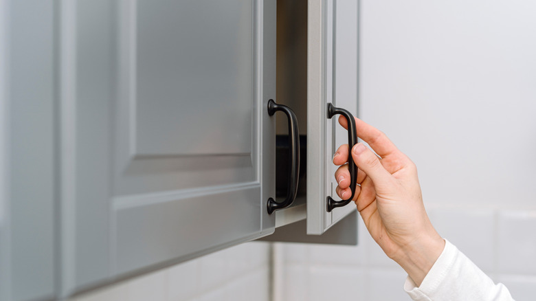 Closeup of person's hand closing a kitchen cabinet door