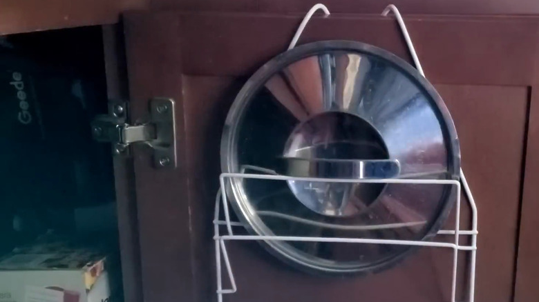 Shower caddy hanging on inside of kitchen cabinet door, with a pot lid in it