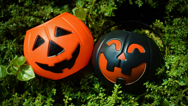 Two Jack-o'-lantern pails in orange and black among green foliage