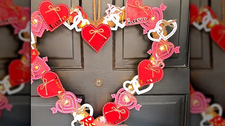 A Valentine's Day wreath wrapped in jute and covered in various themed decorations on a front door