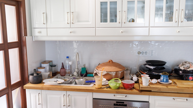 Cluttered kitchen counter with lots of dishes and white upper cabinets