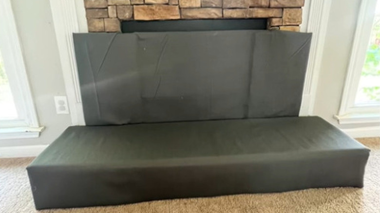 A gray padded cushion covering the fireplace opening and hearth for child safety.