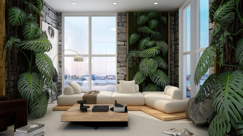 A light-filled living room is decorated with a white sectional couch and oversized plants.