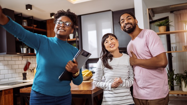 A smiling interracial couple works with an African American interior designer inside their home.
