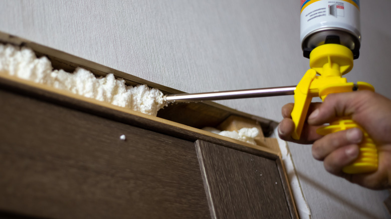 A person's using spray foam to insulate around a framed space