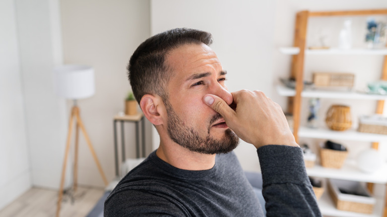 Man pinching nose to avoid bed smell in home