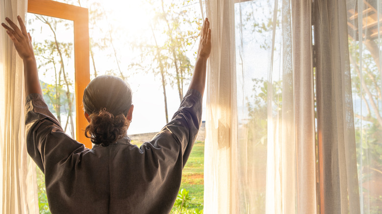 Woman opening her wood-framed windows to let in fresh air.