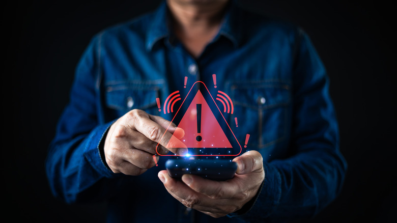 A man's phone is sending him an alert, symbolized by a glowing red caution sign