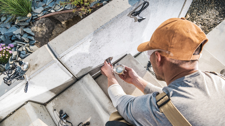 A landscaper is shown in an overhead shot installing a small uplight near a concrete stair