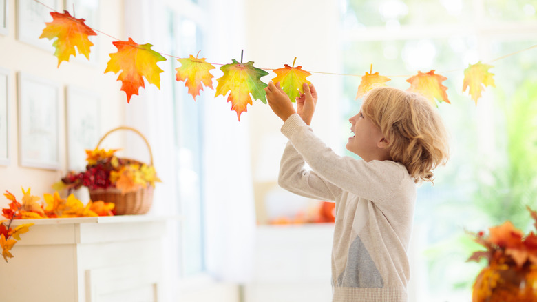 A child with short blond hair decorates a living room for fall.