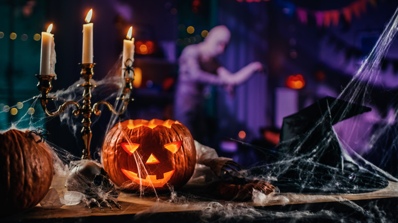 A moody cobweb-covered Halloween display with candelabra, jack-o'-lantern, and witch's hat
