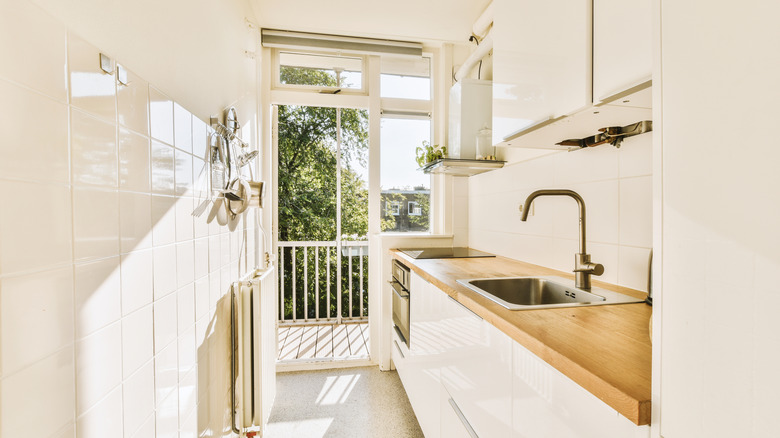Small kitchen featuring light shades on backsplash and wood countertops, near an open window and balcony