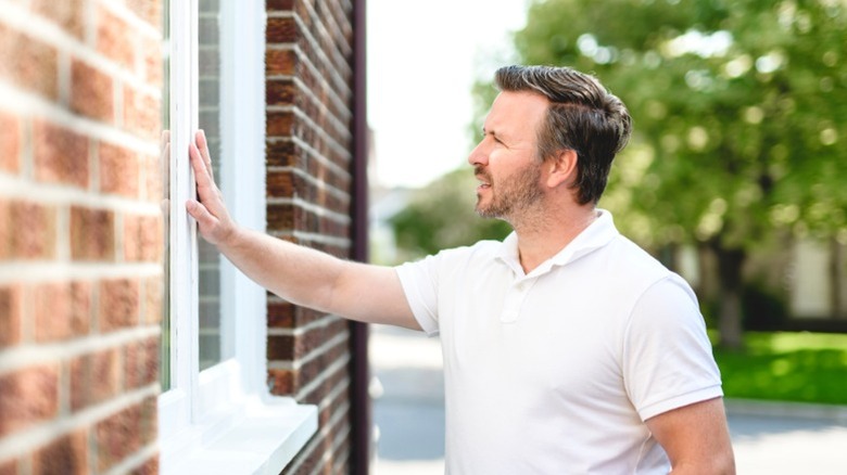 Man checking window from outside during day to gauge burglar access