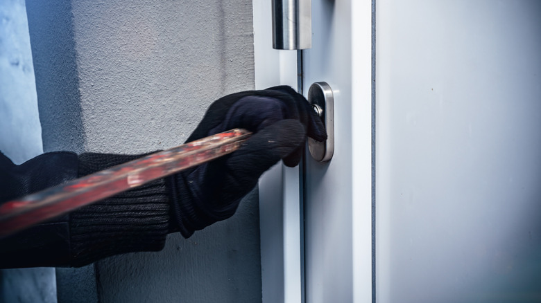 Gloved hand holding a crowbar breaking into a home