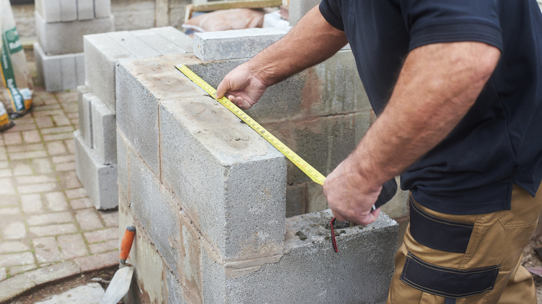 A man's hands measuring cinder blocks.