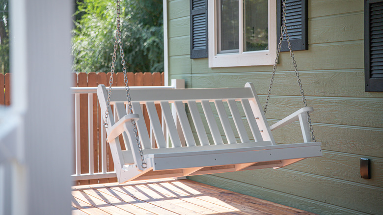 white porch swing hanging in front of green house