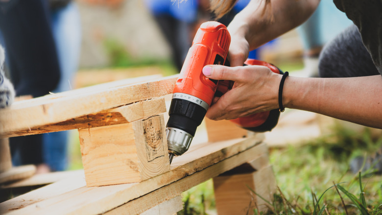 Person using drill on wood pallet outside