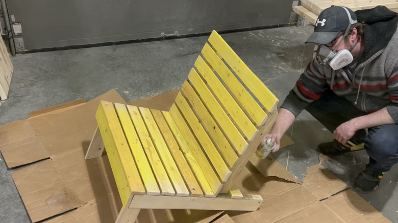 A man spray painting pallet chairs