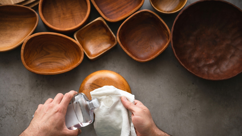Person's hands holding oil and a white cloth about to polish wood bowls