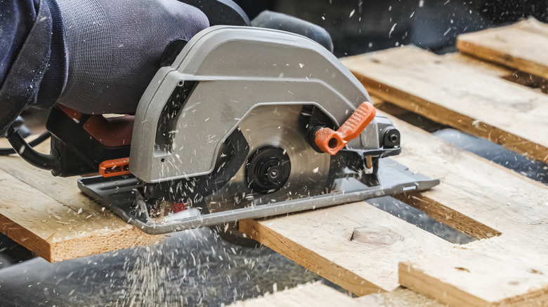 A man sawing through old wood pallets to make furniture