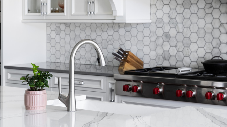 A white and gray kitchen with marble countertops and tile backsplash.