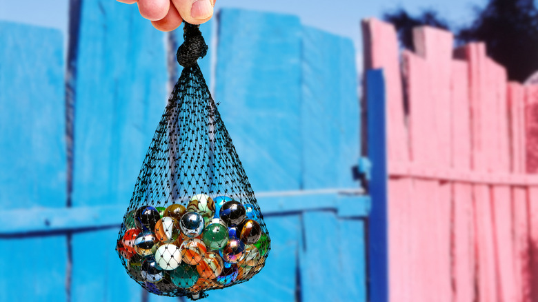 A person holding a bag of marbles in front of a colorful wood fence