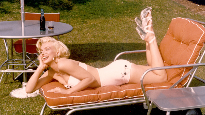 Marilyn Monroe smiling and lying on an outdoor chaise lounge chair