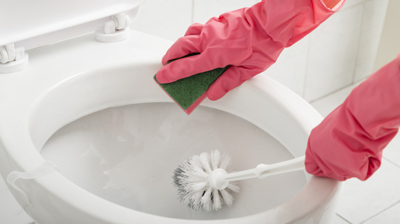 Person wearing gloves cleanig toilet bowl.