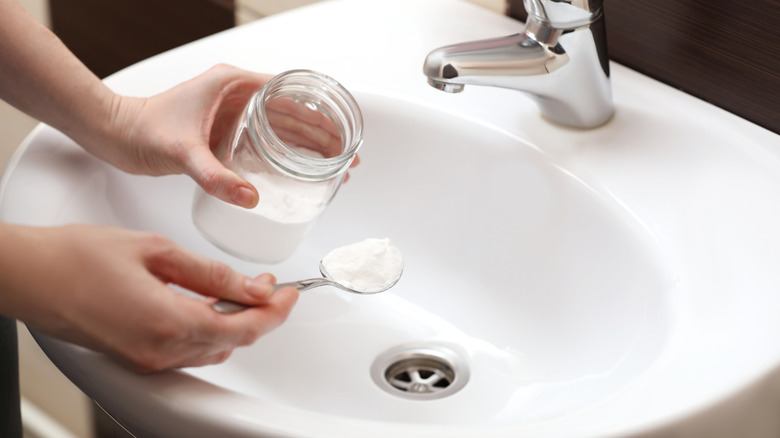 Hands spooning baking soda into bathroom sink.