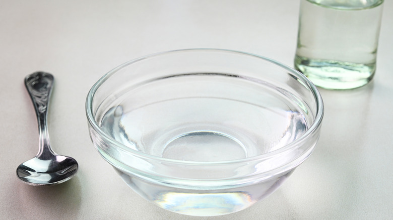 White vinegar in a glass bowl next to a spoon