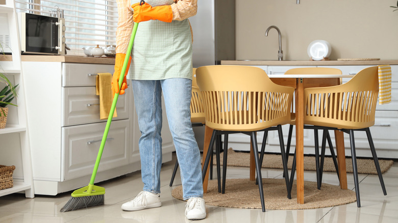 A woman sweeps a kitchen floor.