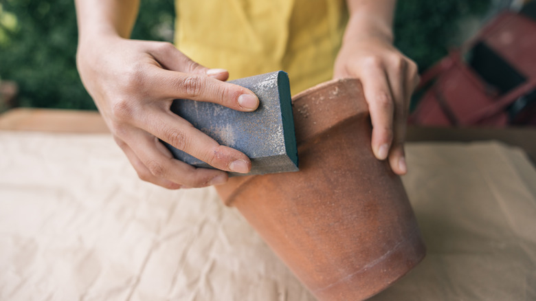 A hand scrubbing a terra cotta clay pot.