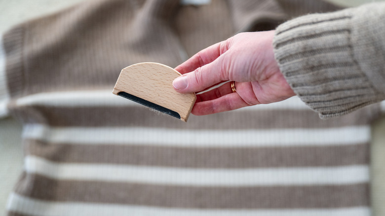 Woman's hand holding a fabric comb above a striped sweater