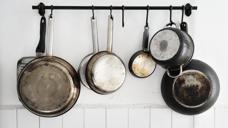 A wall-mounted railing with pots and pans hanging via hooks.