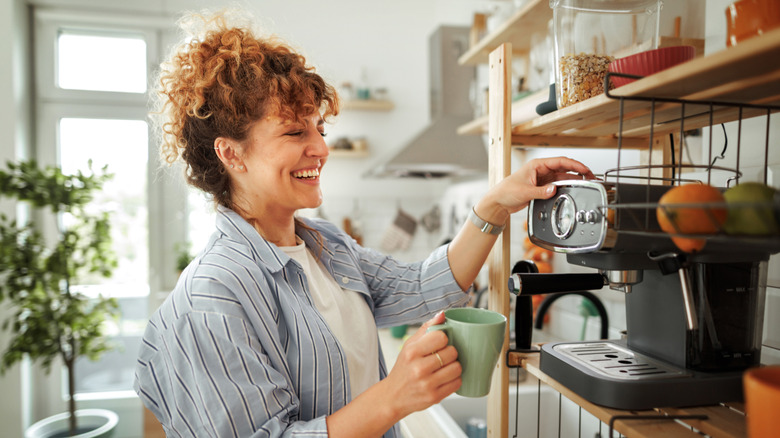 Smiling woman in a blue striped shirt preparing to make a cup of coffee.