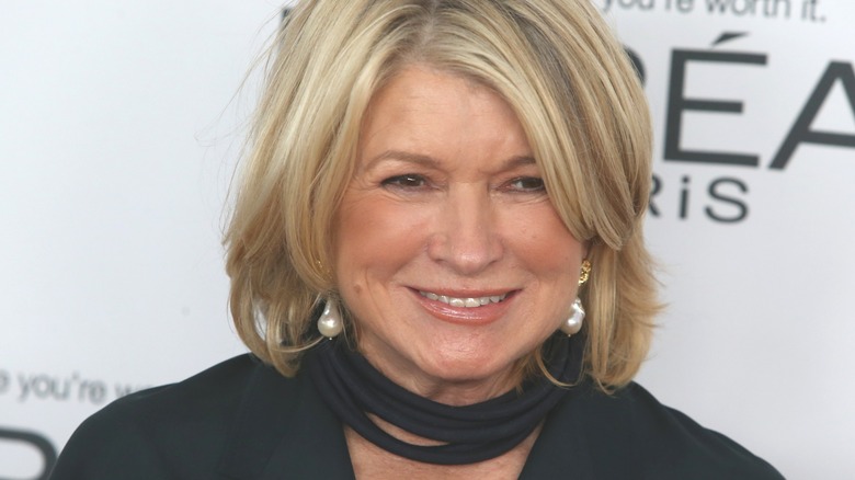 Martha Stewart standing in front of an ad banner, posing for photos with a black outfit on and large pearl earrings