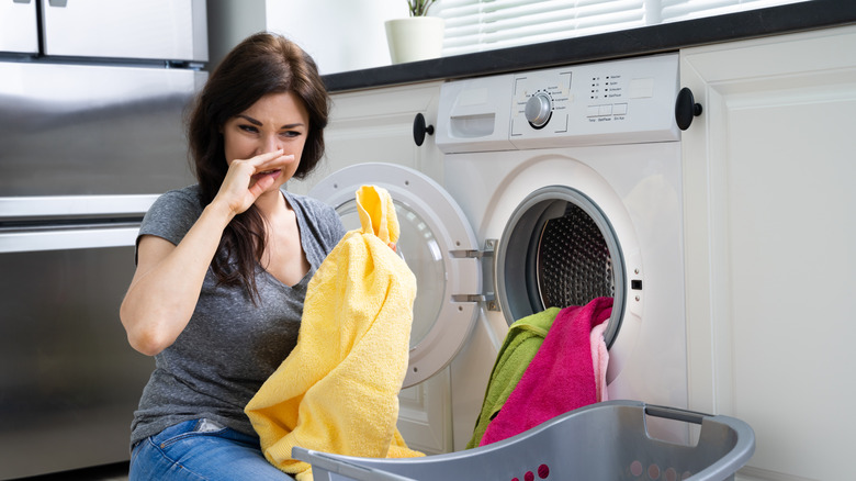 Woman holds nose pulling out smelly laundry from washer.