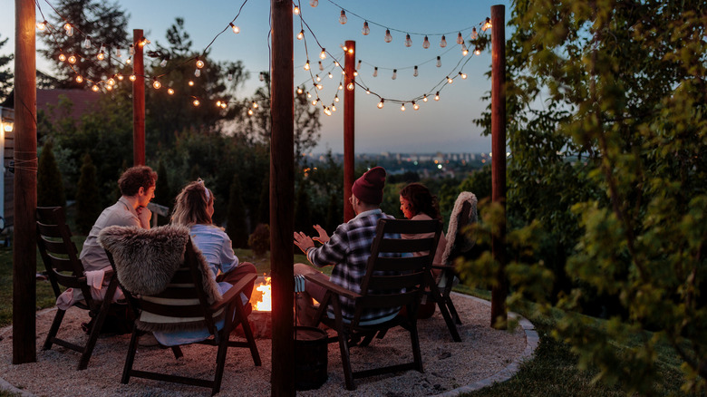People sitting in a backyard under a set of string lights.