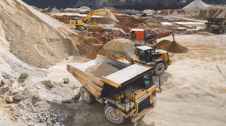 Trucks and machines work inside a quarry.